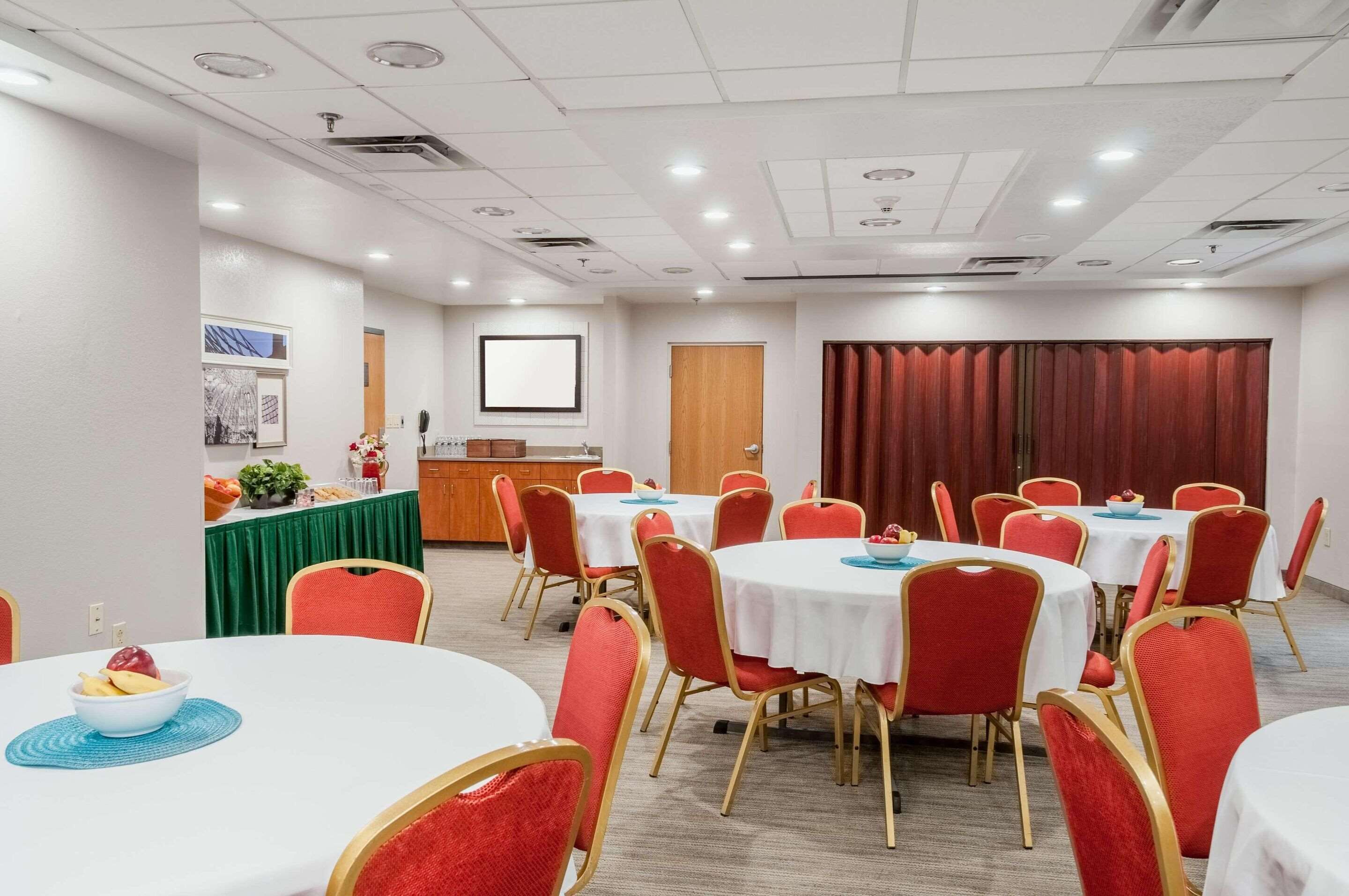 A conference room with round tables, red chairs, a projector screen, and a green table with food.