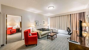 Een hotelkamer met een rode fauteuil, een bank, een salontafel, een televisie en een bureau met een lamp.