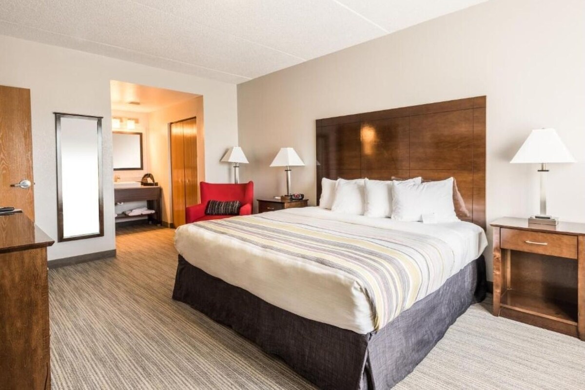 Een hotelkamer met een groot bed, een houten hoofdbord, twee nachtkastjes met lampen, een rode stoel en een garderobe.
