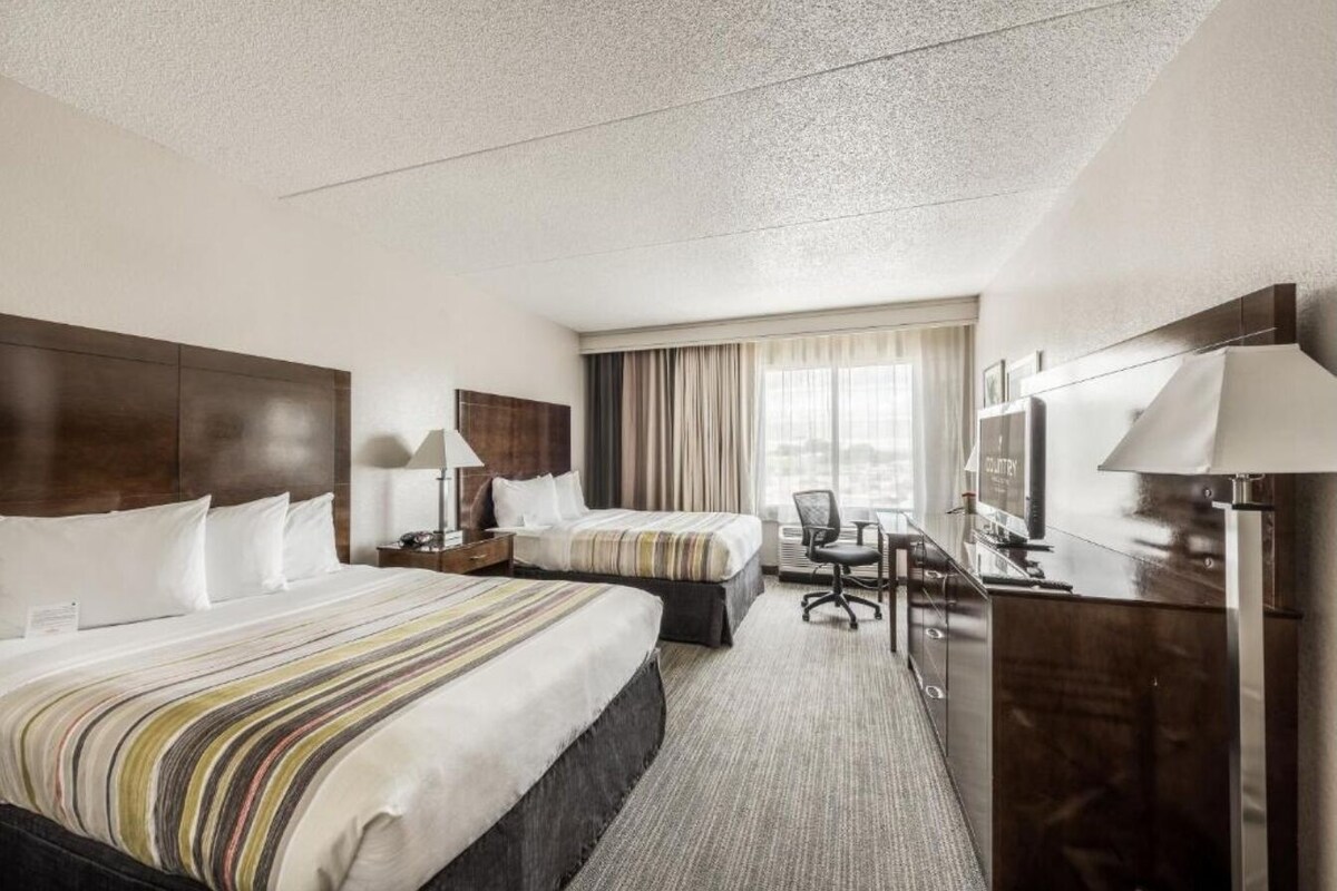 Een hotelkamer met twee bedden, een bureau, een stoel, een televisie en een raam met gordijnen.