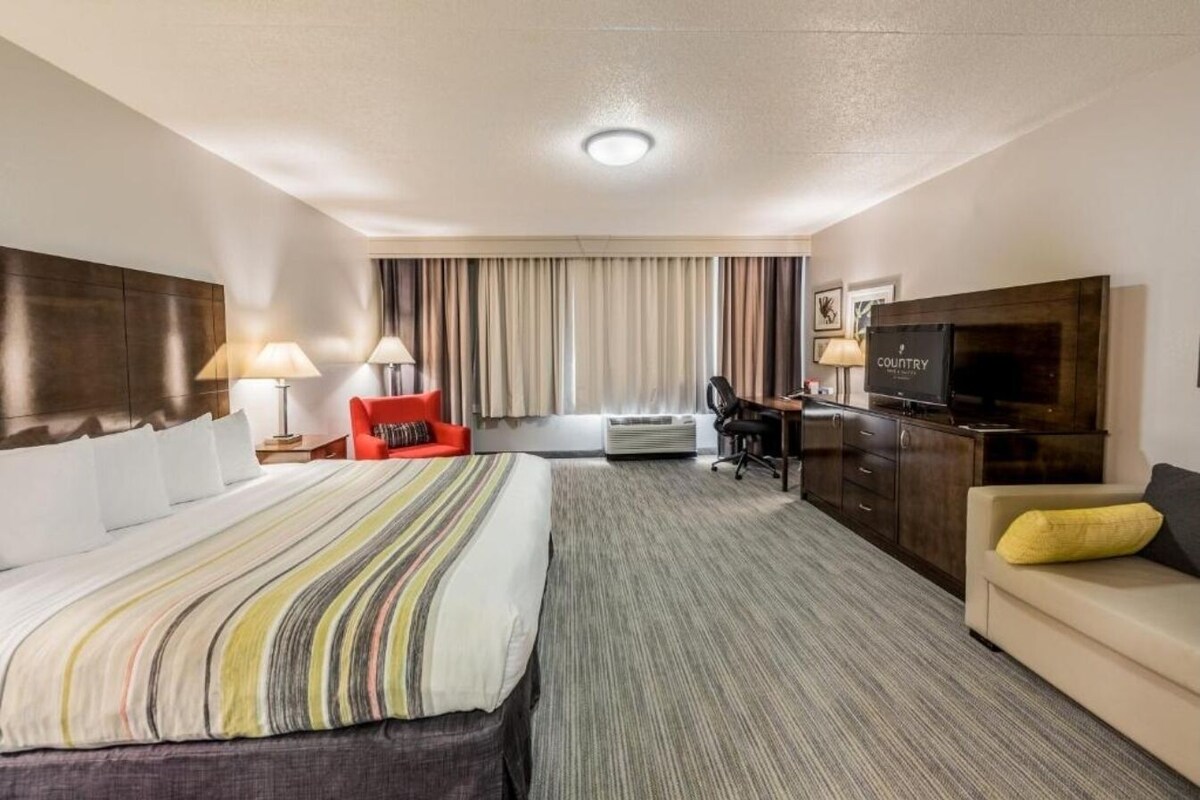 Een hotelkamer met een groot bed, een bureau met een televisie, een rode stoel en een bank.