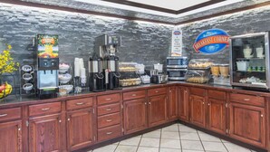 A breakfast area with a coffee machine, a juice dispenser, and a variety of food items on a counter.