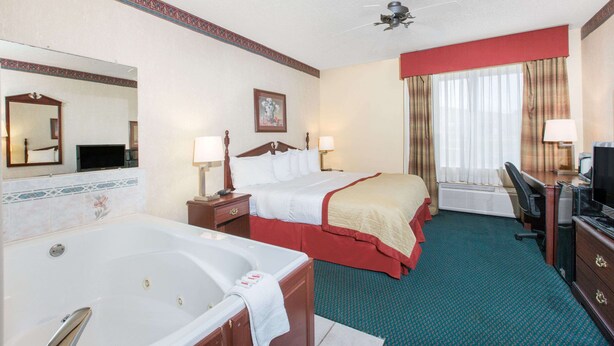 A hotel room with a large bed, a smaller bed, a desk with a chair, a television, a mirror, and a window with curtains.