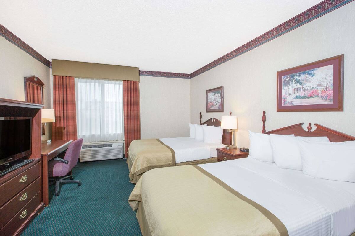 Een hotelkamer met twee bedden, een bureau met stoel, een televisie en een raam met gordijnen.
