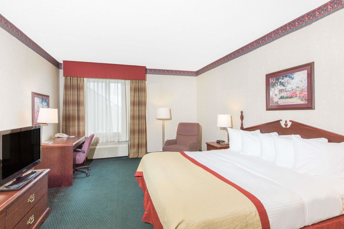 Hotelkamer met een bed, een bureau met een computer, een stoel, een televisie en een raam met gordijnen.