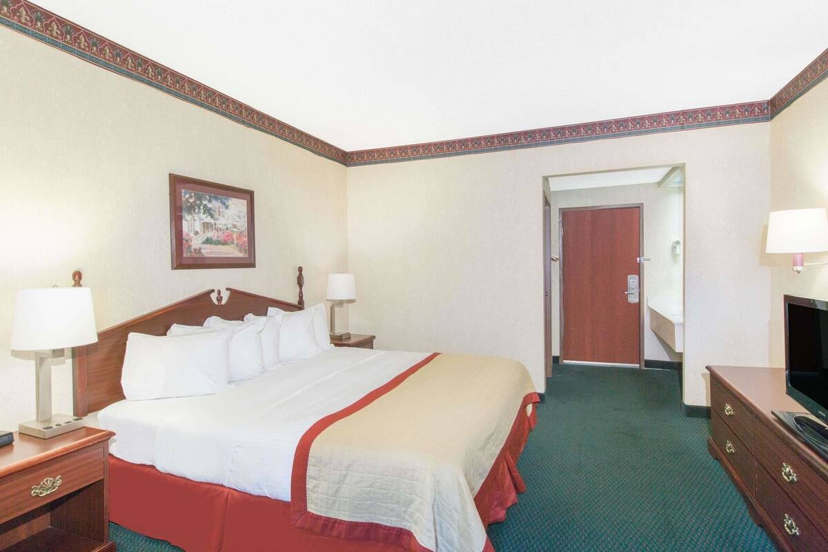 Een hotelkamer met een bed, nachtkastjes, een televisie en een deur die naar een andere kamer leidt.