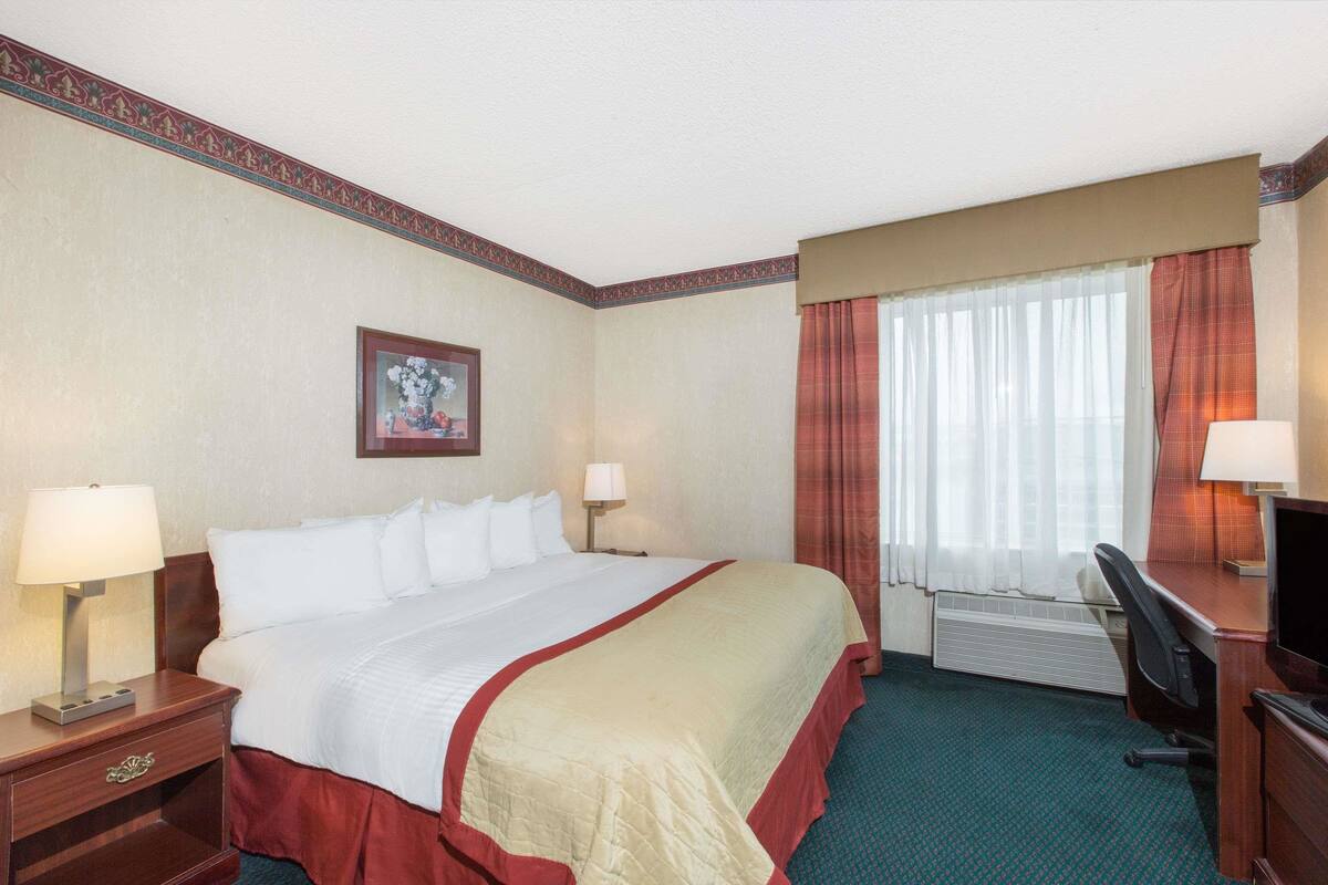 Een hotelkamer met een groot bed, twee nachtkastjes met lampen, een bureau met stoel, een televisie en een raam met gordijnen.
