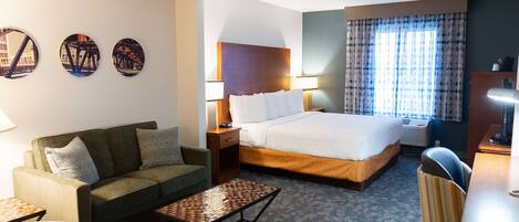 A hotel room with a bed, a sofa, a desk, and a small table. There are three wall art pieces above the sofa.