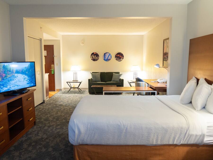 A hotel room with a bed, a TV, a desk, a chair, and a lamp.