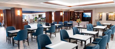 A spacious dining area with multiple tables and chairs, a television, and a bookshelf.