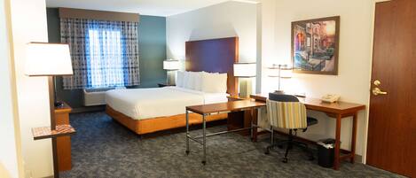 A hotel room with a bed, desk, chair, and a painting on the wall.
