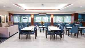 A spacious dining area with multiple tables and chairs, large windows, and a central decorative plant. - La Quinta Inn & Suites by Wyndham Bannockburn-Deerfield (Deerfield)