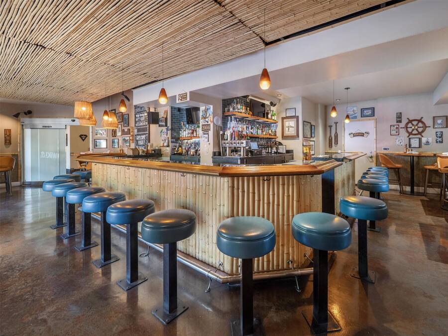 Uma área de bar com banquetas, balcão e prateleiras cheias de garrafas.