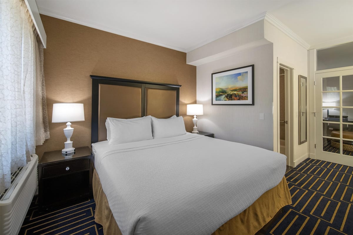 A hotel room with a large bed, two bedside tables with lamps, a painting on the wall, and a door leading to a closet.