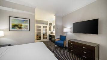 Habitación de hotel con cama, televisor, silla, cómoda y puerta que da a un baño.
