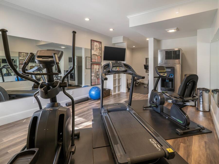 Un gimnasio en casa con cintas de correr, una elíptica, una bicicleta estática y una máquina de remo.