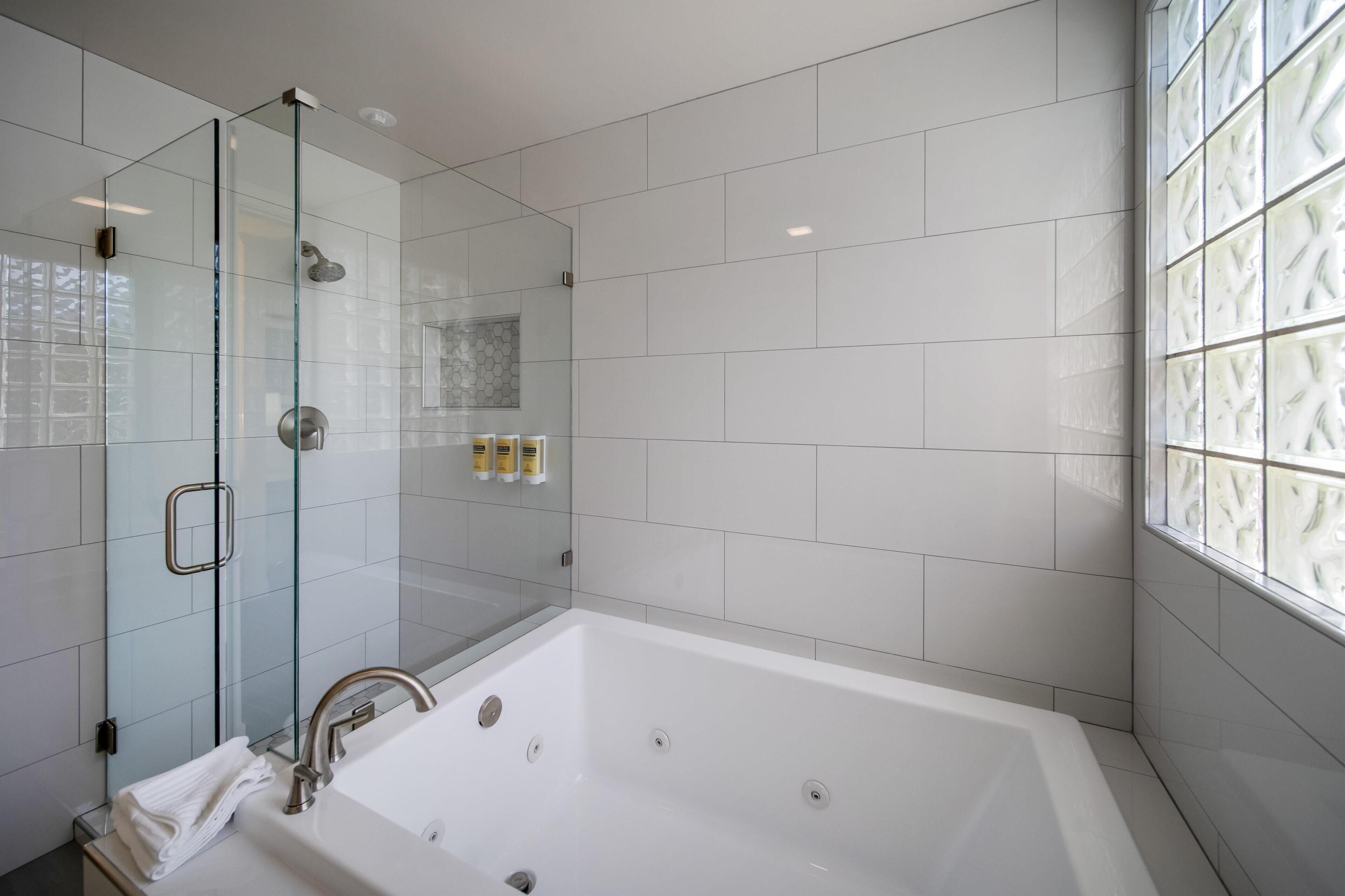Un baño moderno con ducha de vidrio, una bañera blanca grande y una ventana con vidrio emplomado.
