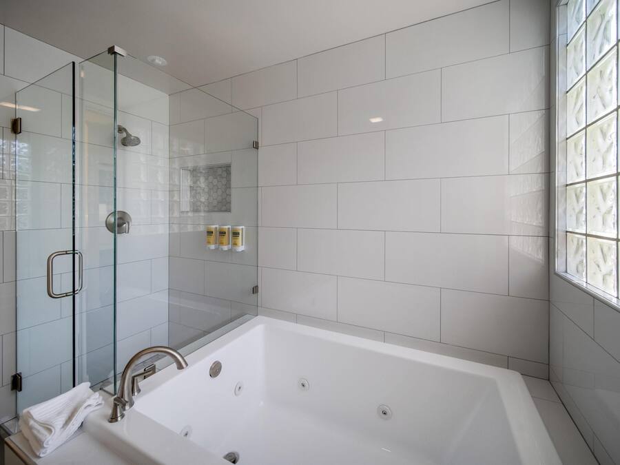 Un baño moderno con ducha de vidrio, una bañera blanca grande y una ventana con vidrio emplomado.