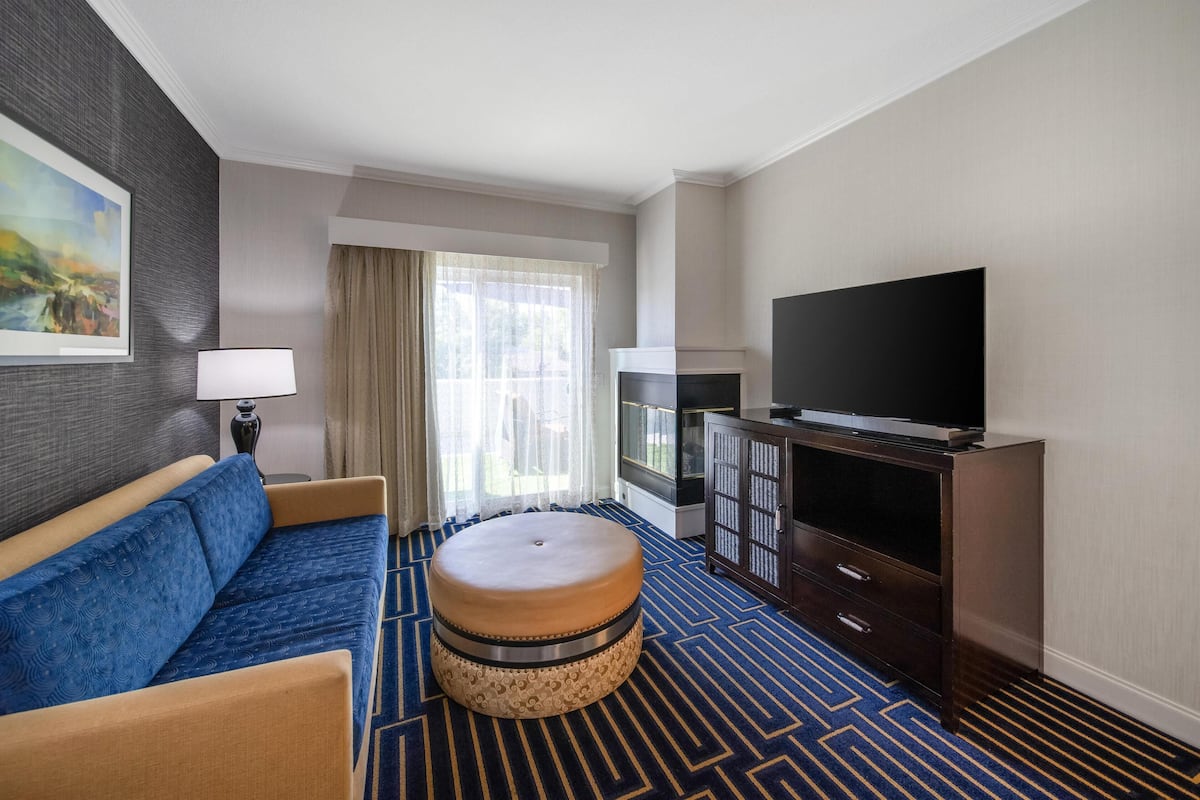 A hotel room with a sofa, ottoman, TV, and a cabinet.