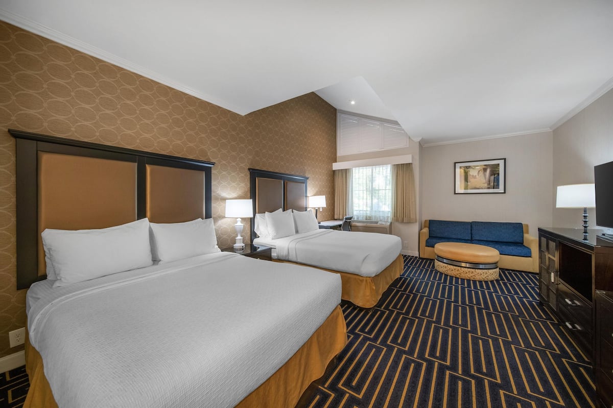 A hotel room with two beds, a sofa, a TV, and a window with curtains.
