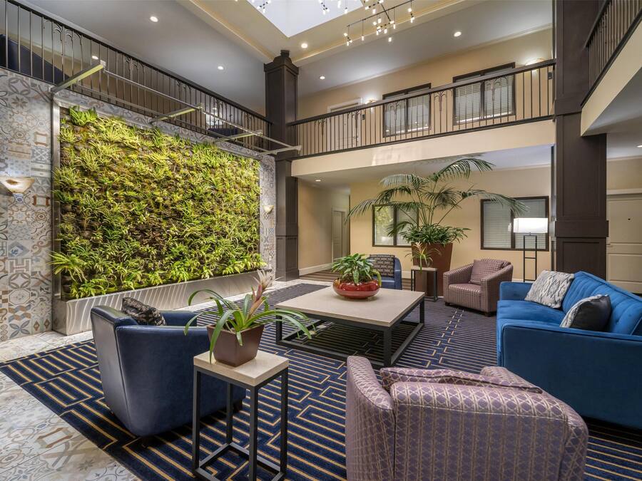 A spacious lobby with a high ceiling, a green vertical garden, comfortable seating, and a modern staircase.