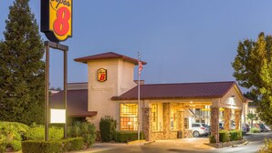 A Super 8 hotel with a stone facade, a red roof, and a parking lot with several cars. - Super 8 by Wyndham Corning (Corning)