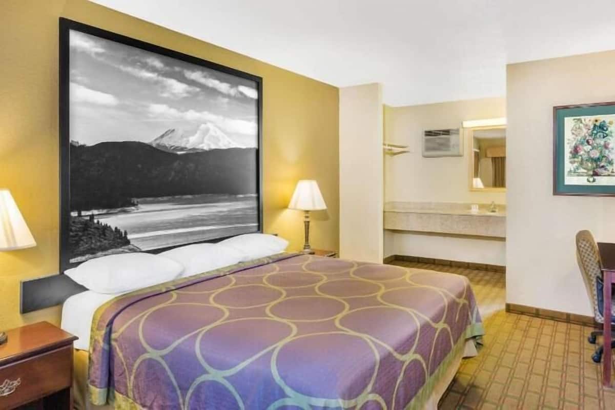 A hotel room with a bed, two bedside lamps, a desk with a chair, a mirror, and a framed picture on the wall.