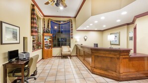 A reception area with a wooden desk, computer, and chair, a large window with curtains, and a clock on the wall. - Super 8 by Wyndham Corning (Corning)