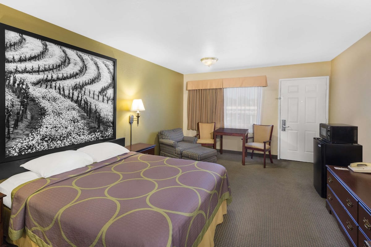 A hotel room with a large bed, a desk, two chairs, a television, and a door.
