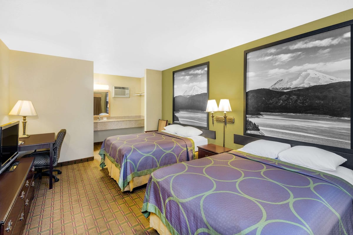 A hotel room with two beds, a desk, a chair, a TV, and a large framed picture of a mountain.