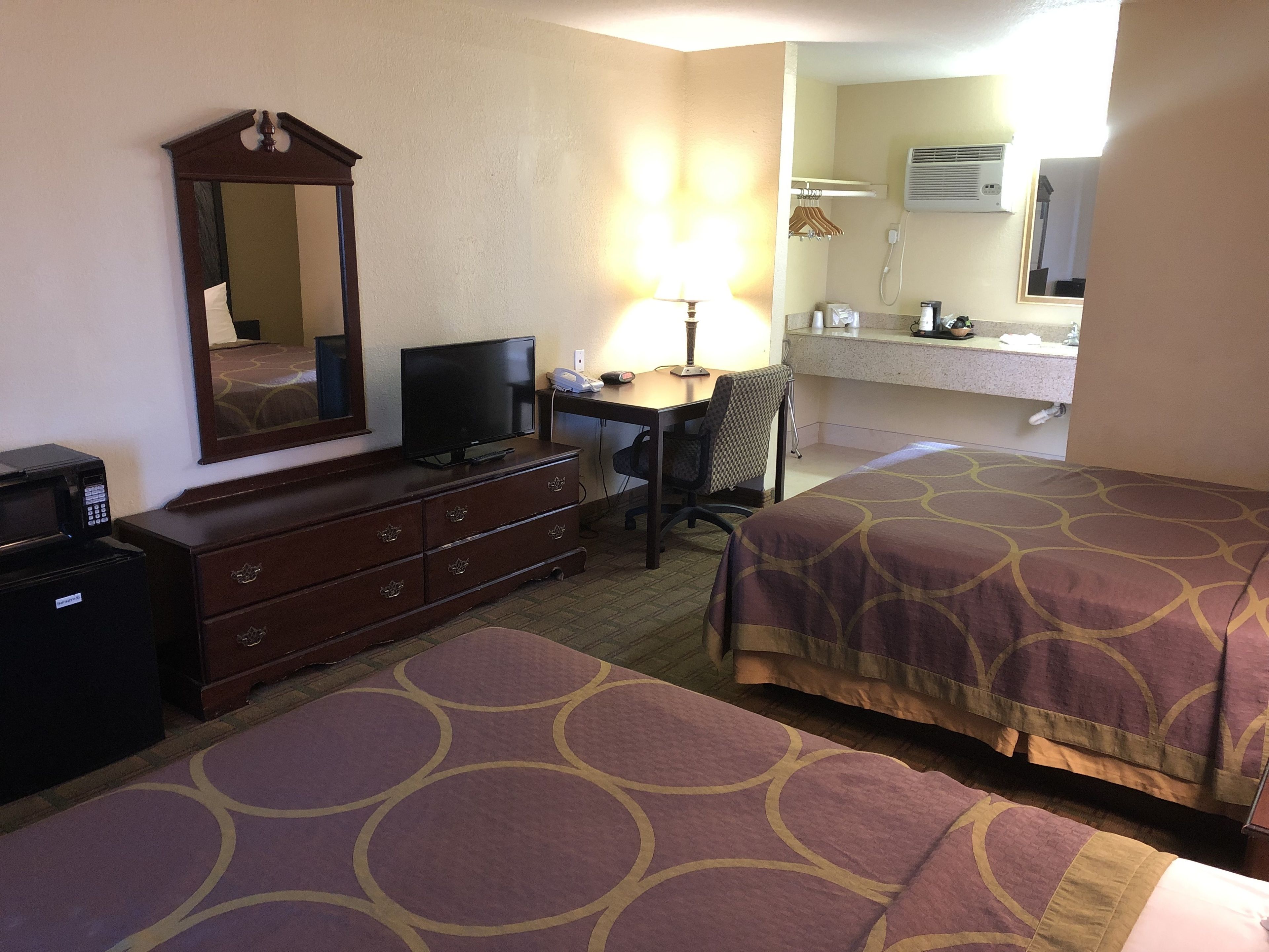Habitación de hotel con cama, escritorio con computadora, cómoda, espejo y baño con lavamanos y espejo.