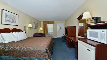 Quarto de hotel com uma cama grande, escrivaninha com micro-ondas, mini-geladeira e espelho.