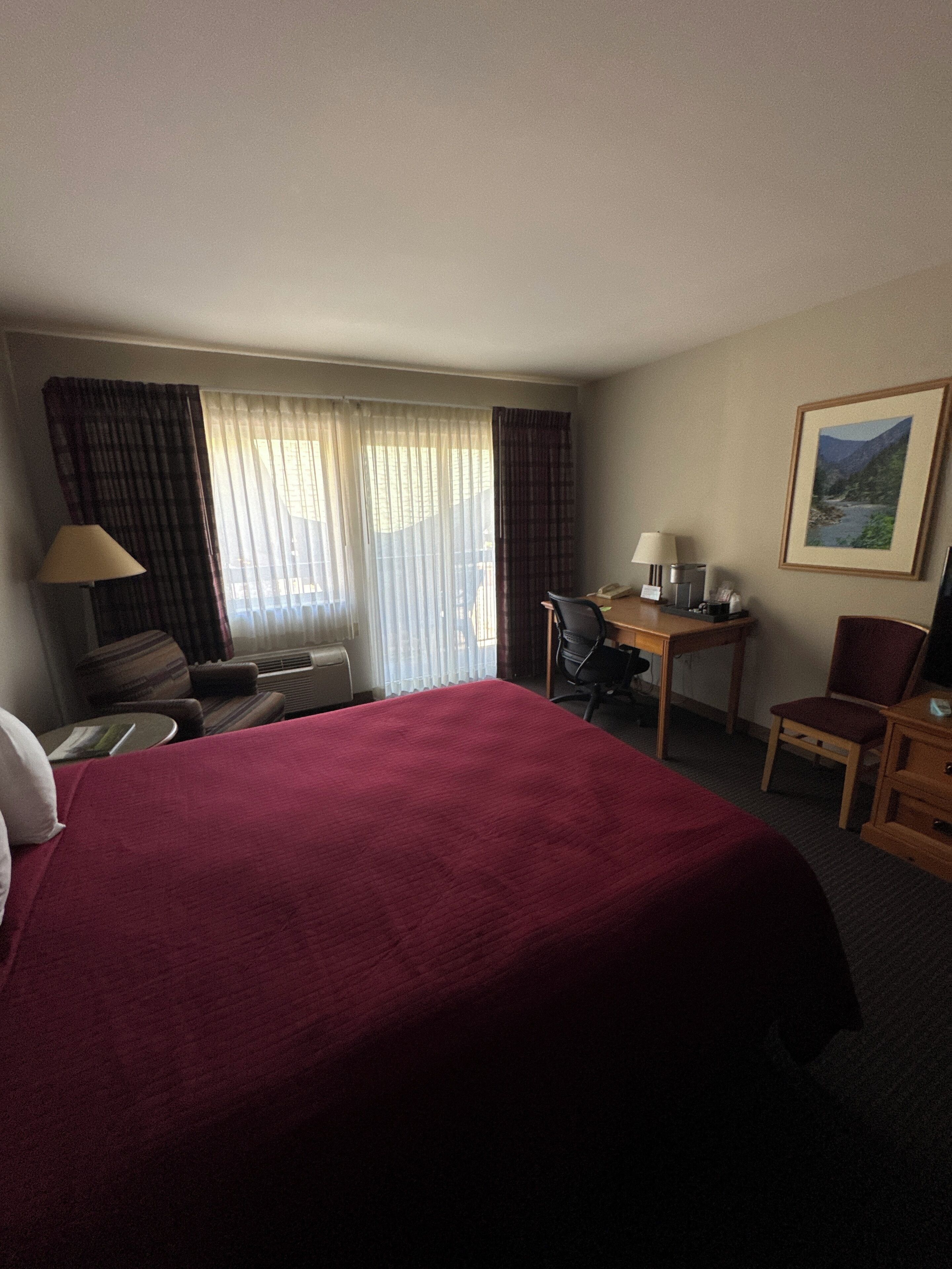Ein Hotelzimmer mit einem großen Bett, einem Schreibtisch, einem Sessel, einer Lampe und einem Bild an der Wand.