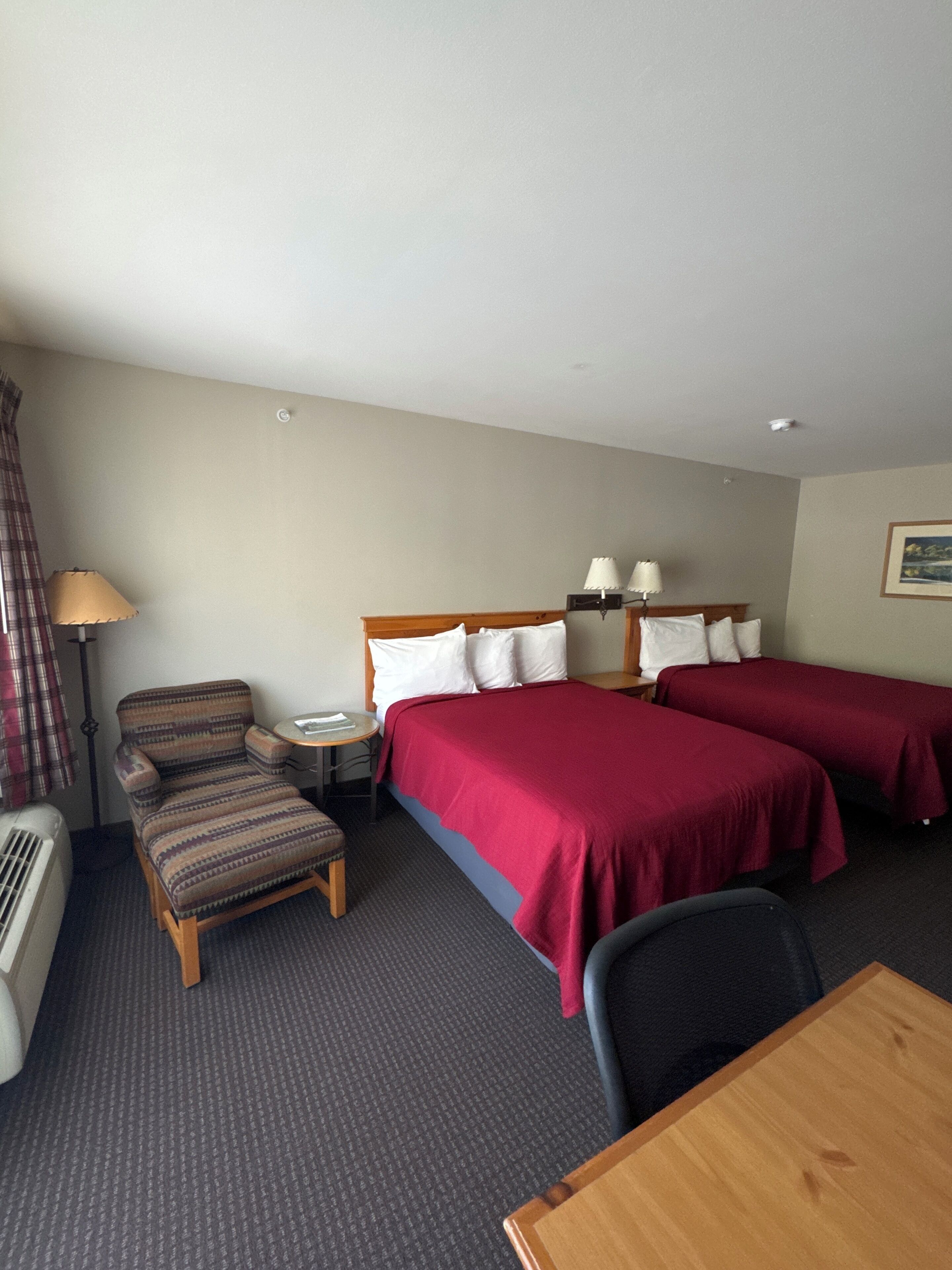 Een hotelkamer met twee enkele bedden, een houten stoel, een klein rond tafeltje, een lamp en een verwarming.