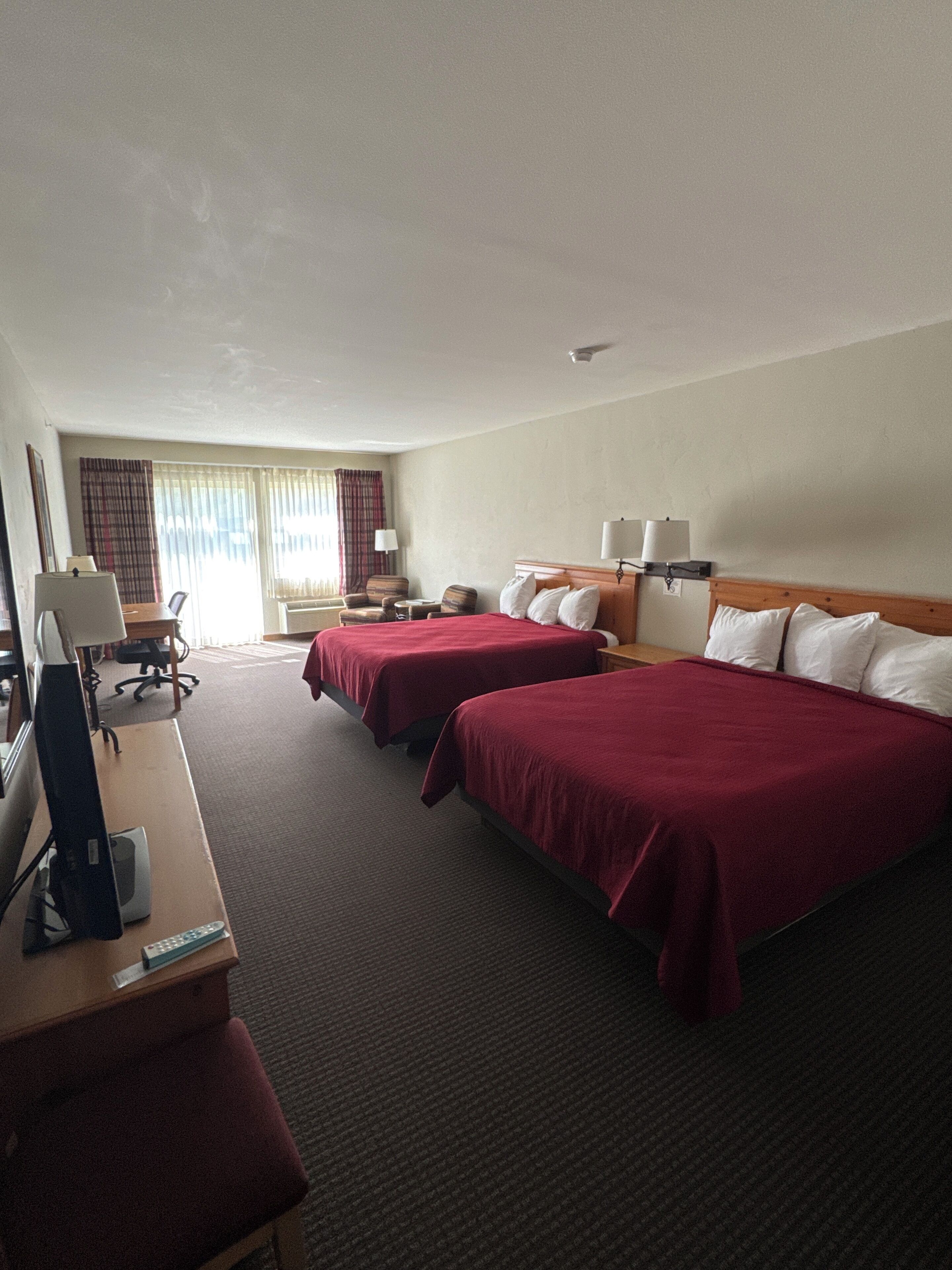 A hotel room with two beds, a desk with a computer, a chair, and a window with curtains.
