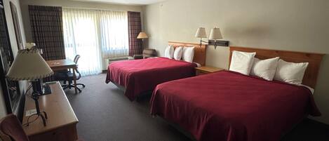 Une chambre d’hôtel avec deux lits, un bureau, une chaise, une lampe et une fenêtre avec des rideaux.
