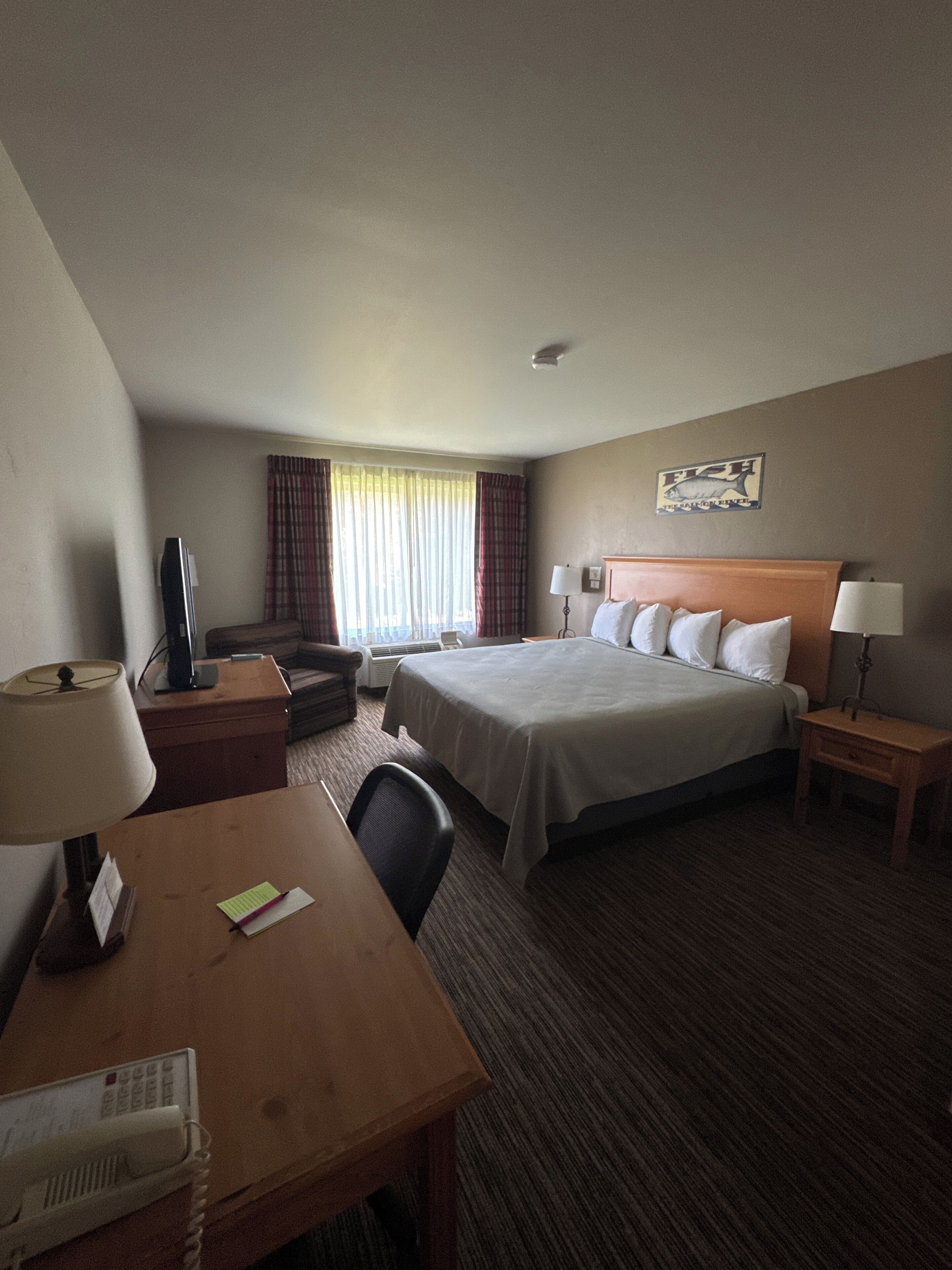 Une chambre d’hôtel avec un lit, un bureau avec un téléphone, une chaise, une télévision et une fenêtre avec des rideaux.