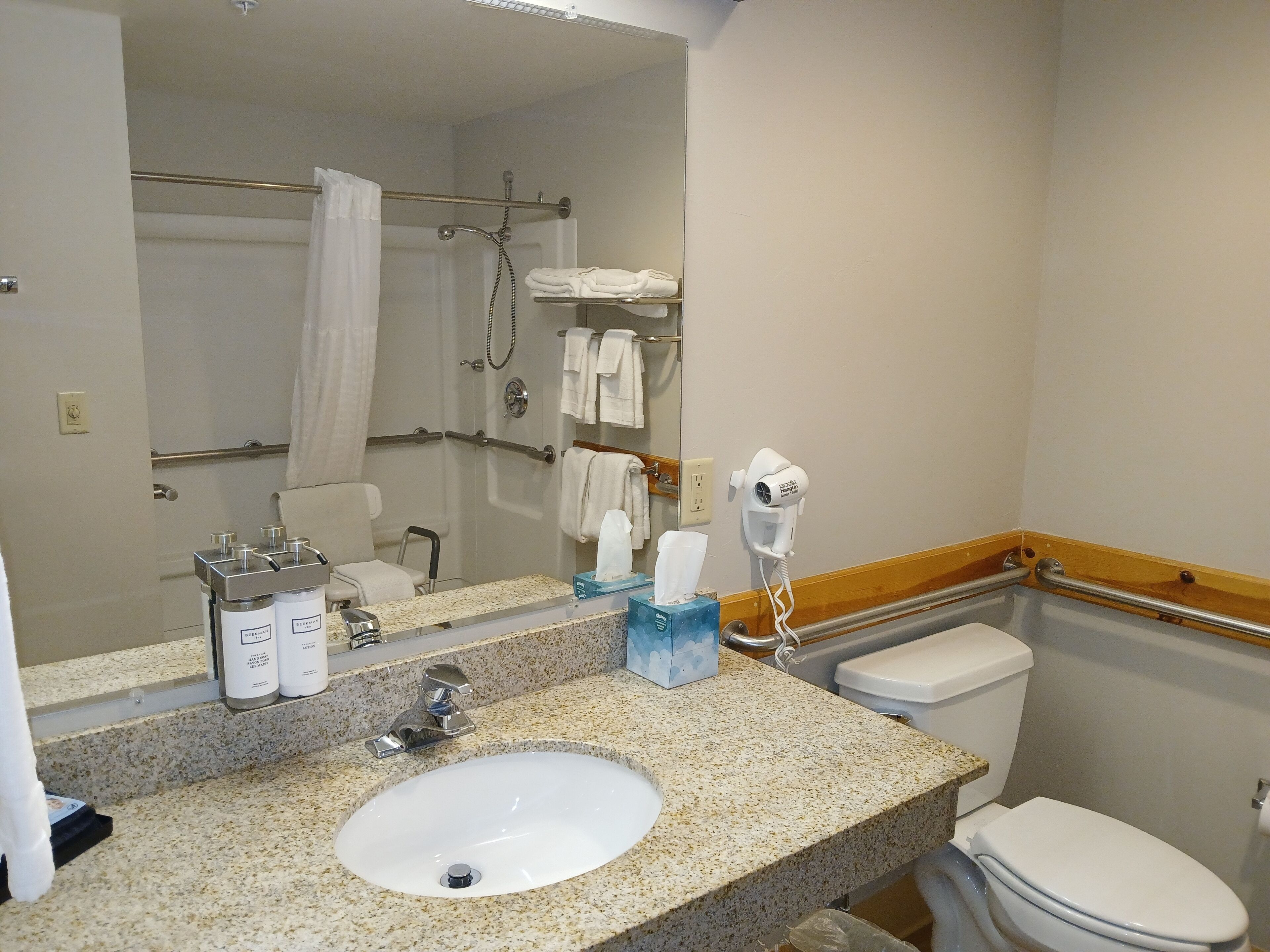 A bathroom with a sink, mirror, towel rack, shower, and toilet.