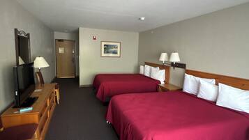 A hotel room with two beds, a desk with a television, and a door.