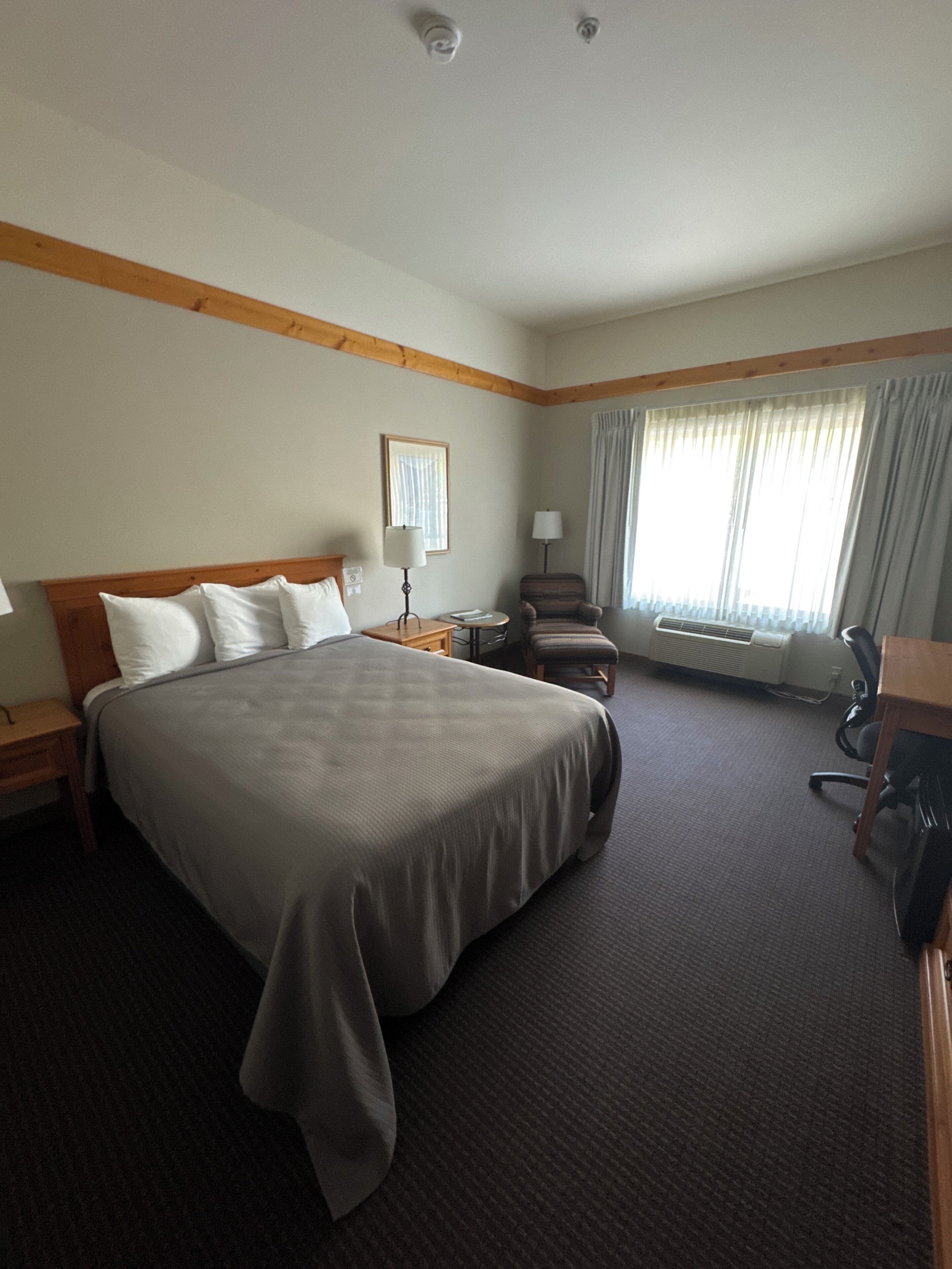 A hotel room with a large bed, a chair, a desk, and a window with curtains.
