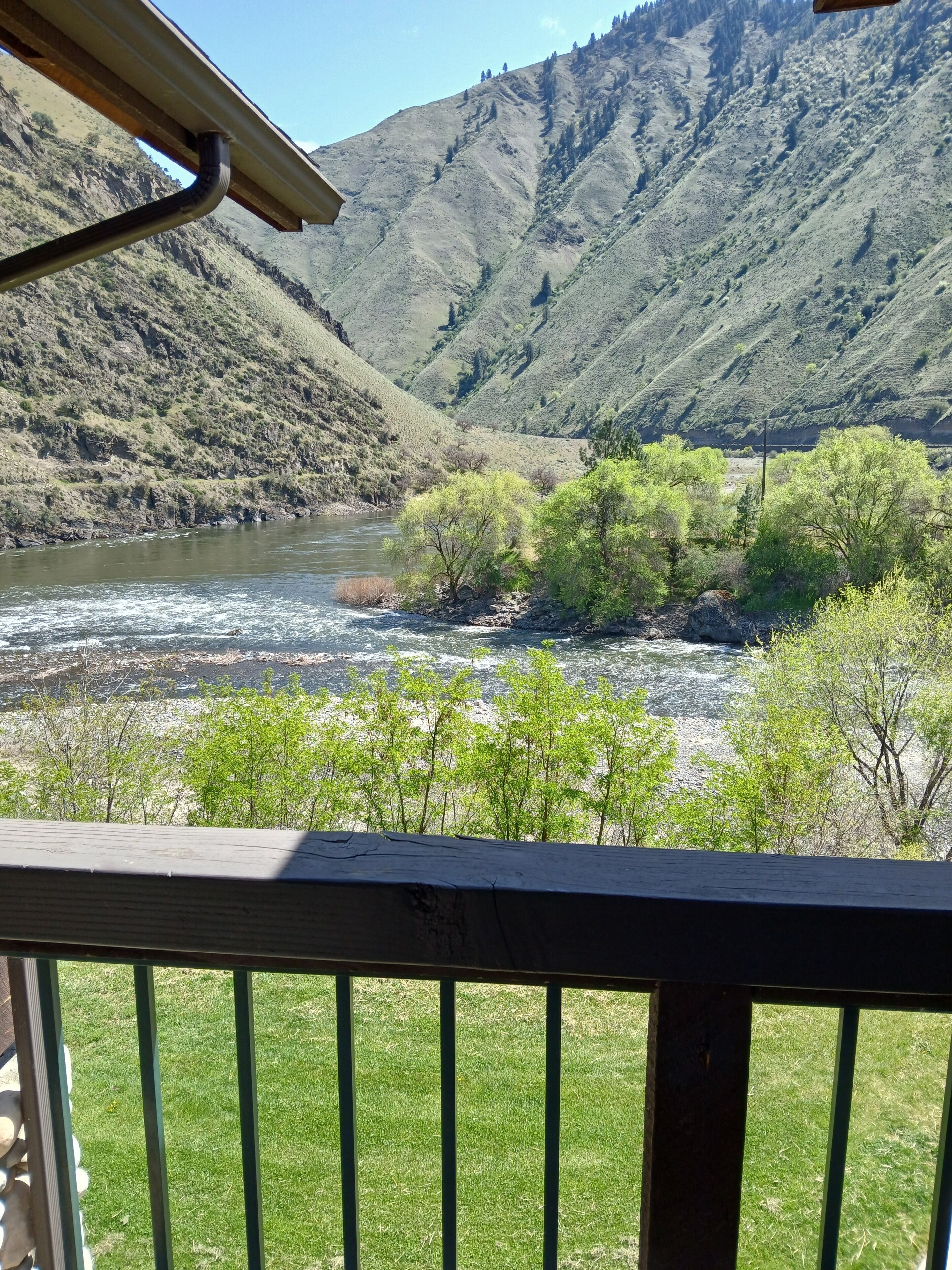 Un río serpentea a través de un paisaje montañoso con vegetación verde y una terraza de madera en primer plano.
