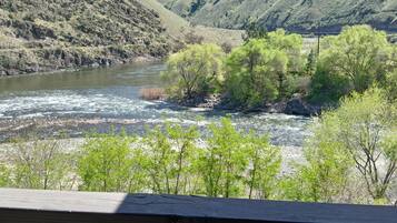 Un río serpentea a través de un paisaje montañoso con vegetación verde y una terraza de madera en primer plano.