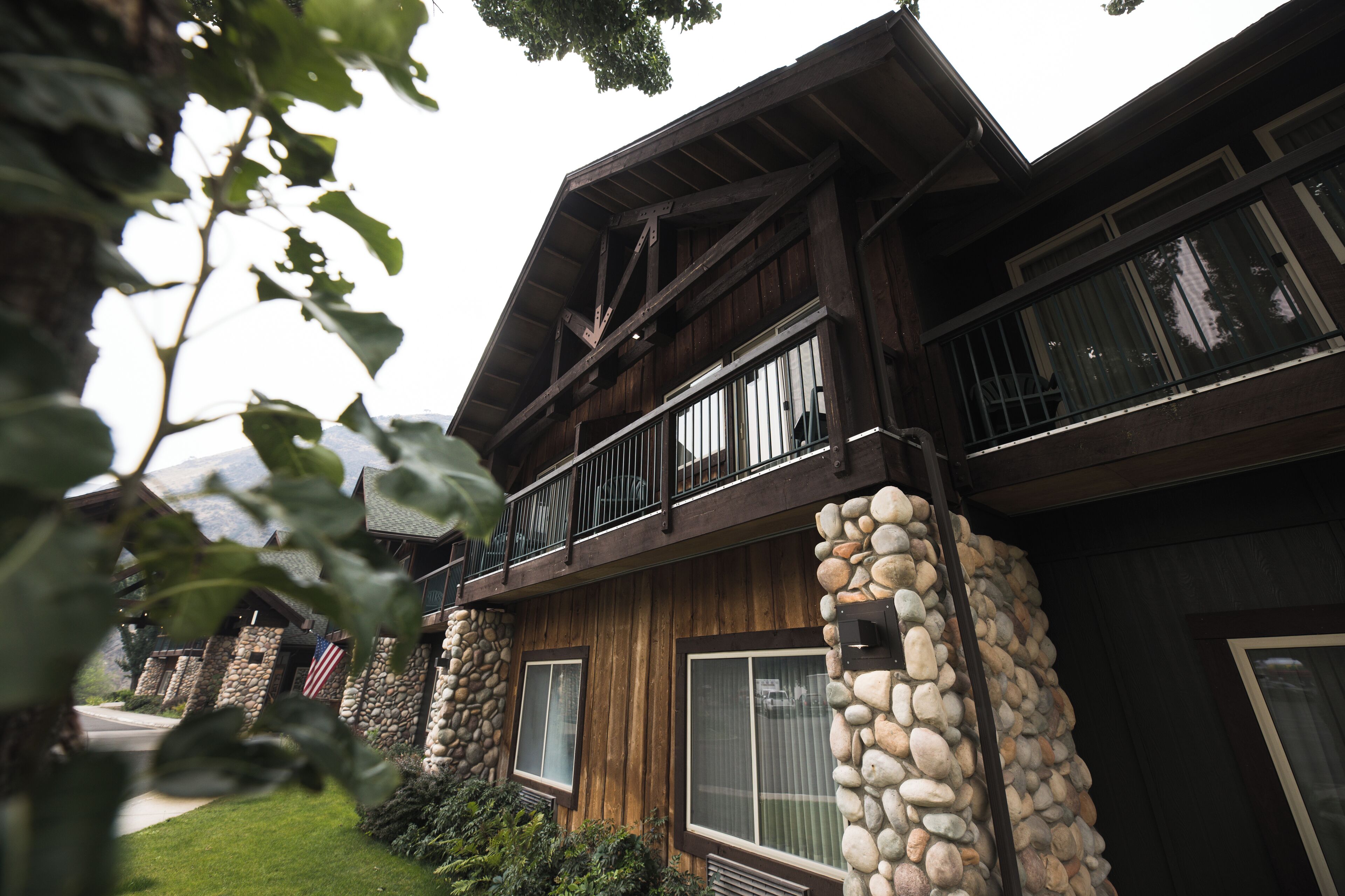 A two-story wooden house with stone pillars, large windows, and a balcony.