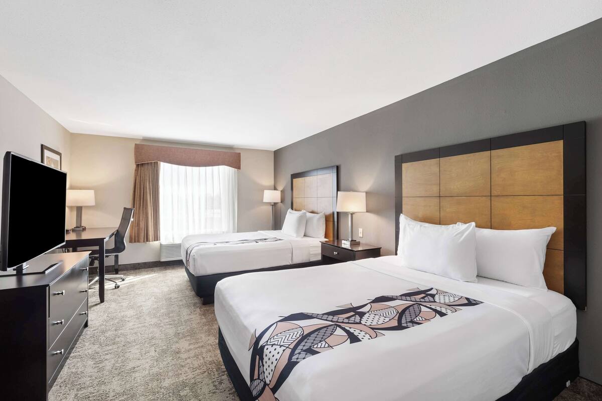 A hotel room with two beds, a TV, a desk, and a chair.