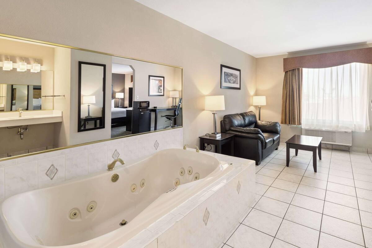 A hotel room with a large bathtub, a sofa, a coffee table, and a desk with a lamp.