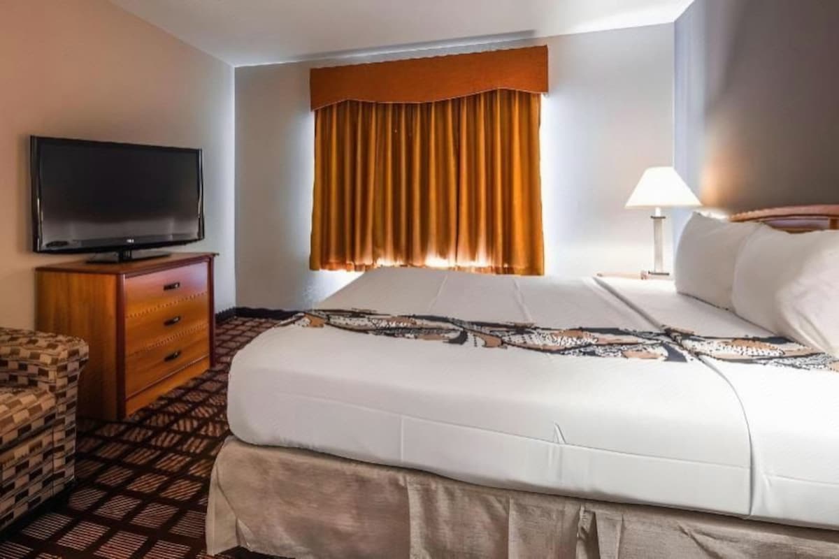 A hotel room with a bed, a television, a chair, a dresser, and a window with curtains.