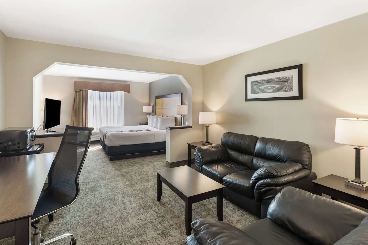 A hotel room with a bed, a leather sofa, a desk with a chair, a coffee machine, and a television.