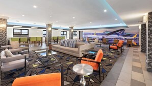 Un'ampia hall dall'arredamento moderno, con un divano grande, diverse poltrone, un tavolino da caffè e un murale raffigurante un aereo.