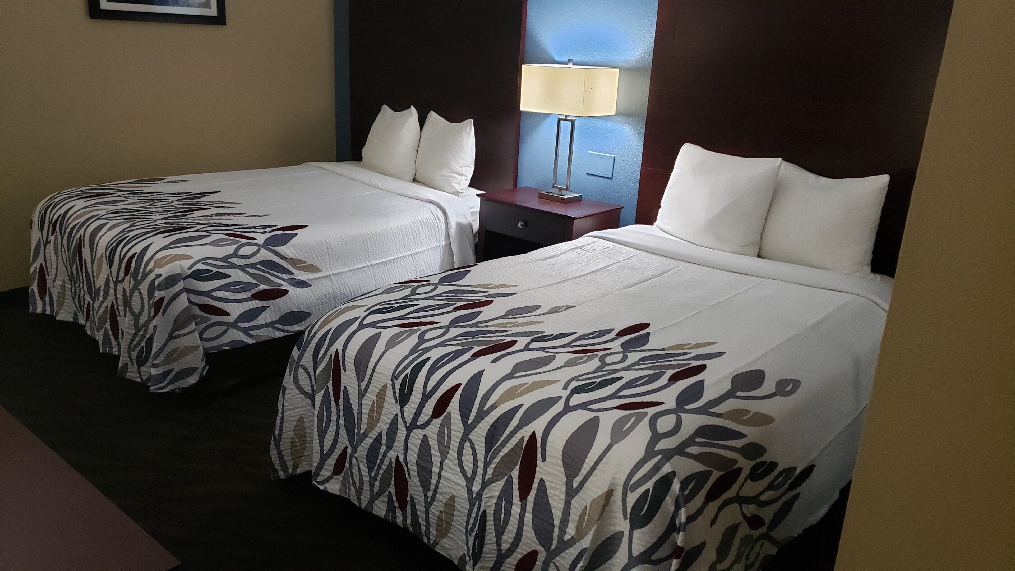 Two twin beds with matching floral bedspreads, a nightstand with a lamp, and a wall-mounted light fixture.