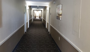 A corridor with a patterned floor, doors on both sides, and a light fixture on the ceiling. - Red Roof Inn Port Allen West LSU Stadium (Port Allen)
